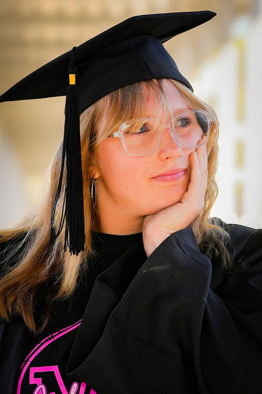 A graduate in cap and gown resting her cheek on her hand